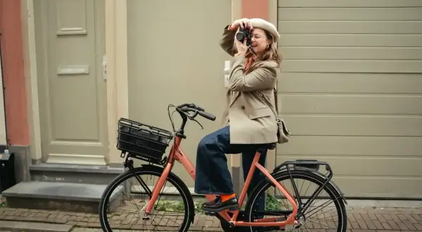 Vrouw met camera op een oranje fiets, klaar voor de beste elektrische fiets 2026.