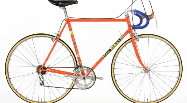 Klassieke racefiets in fel oranje, met "Eddy Merckx" op de buis. Een iconisch stukje fietsgeschiedenis.