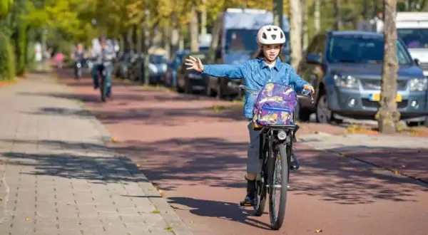 Meisje op fiets met rugzak en helm geeft richting aan, een voorbeeld van verkeersregels voor fietsers.