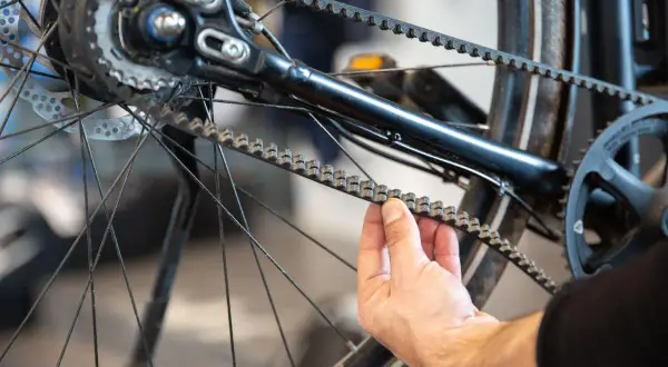 Hand controleert de riem van een fiets, mogelijk ter voorbereiding op het vervangen van de riem fiets.