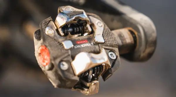 Close-up van een vuil racefiets pedaal met een carbon X-Track Race kliksysteem, klaar voor de volgende rit.