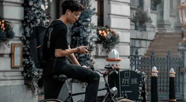 Jonge man op fiets met rugzak, kijkend op zijn telefoon. Is een fietser altijd beschermd in het verkeer?
