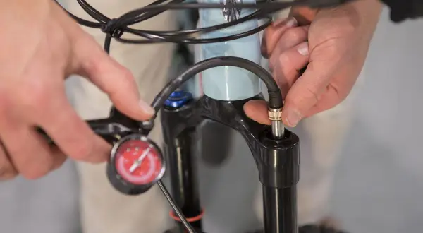 Iemand stelt de verende voorvork van een e-bike af met een pomp en manometer.