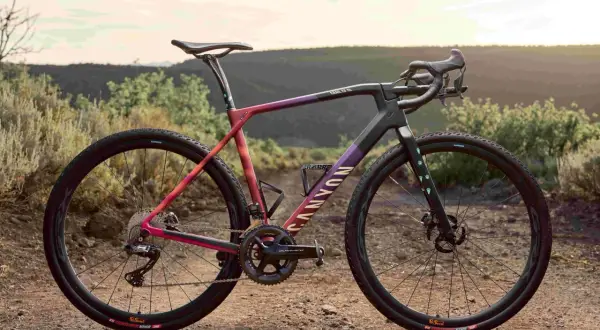 Een kleurrijke Canyon fiets, ideaal voor cyclocross vs gravel bike avonturen, staat in een droog, heuvelachtig landschap.