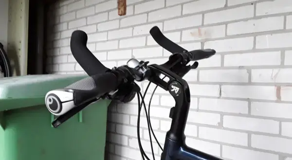 Stuur van een fiets met handvatten en een bel. Geen mountainbike bar ends te zien, wel een groene bak ernaast.
