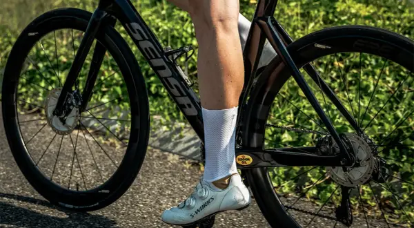 Een wielrenner met witte sokken en schoenen, op een racefiets met hoge velgen. De fiets is zwart met een Sensa frame.
