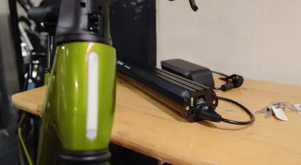 Een groene e-bike frame staat naast een Bosch accu die aan het opladen is. De accu heeft groene lampjes die de laadstatus aangeven.