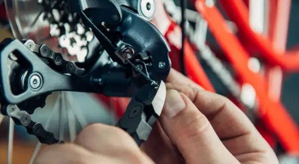 Hand knipt versnellingskabel fiets. De derailleur en ketting zijn zichtbaar, met een rode fietsframe op de achtergrond.