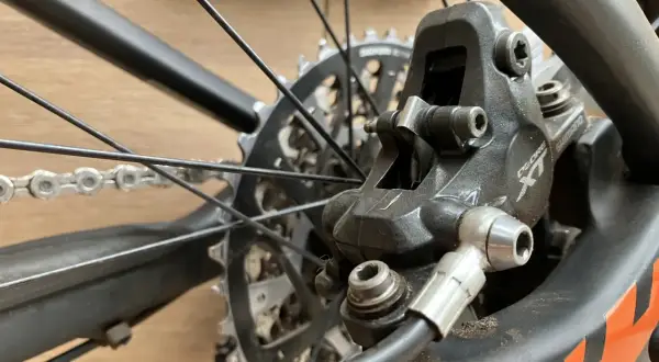 Close-up van een fietsremklauw, klaar voor het bijvullen van hydraulische remmen. De schijfrem en ketting zijn zichtbaar.
