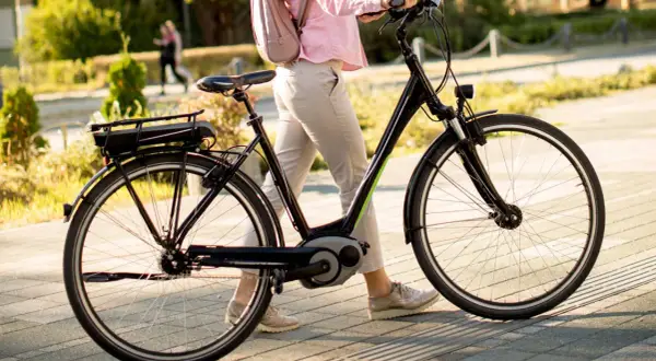 Vrouw loopt met elektrische fiets, de kilometerstand is niet zichtbaar, maar de fiets is klaar voor een rit.
