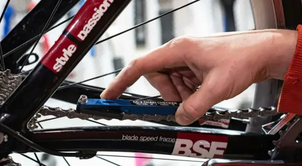 Hand gebruikt een blauwe kettingmeter om te controleren of het tandwiel van de fiets vervangen moet worden.