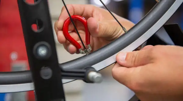 Met een rode spaaksleutel wordt een fietswiel gericht. Een hand draait aan de nippel om het wiel weer perfect rond te maken.