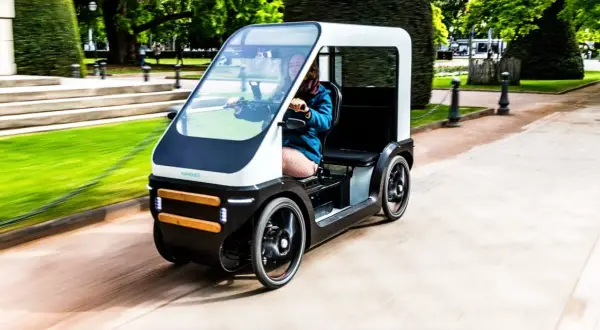 Een vrouw rijdt in een moderne fiets met dak door een park. De fiets heeft een strak design en biedt bescherming tegen het weer.