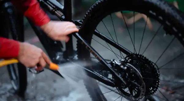 Iemand maakt de fietsketting schoon met Dasty, terwijl de rest van de fiets nat wordt gespoten.