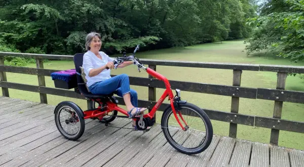 Vrolijke vrouw geniet op een driewieler, een veilige fiets voor ouderen, langs een groen kanaal.