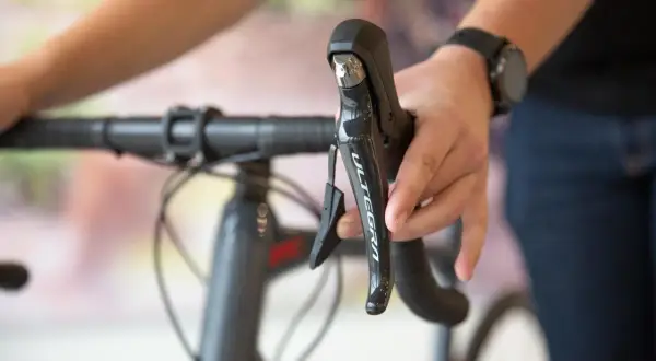 Hand op het schakelen van een racefiets, met de Ultegra-aanduiding zichtbaar op de remhendel.