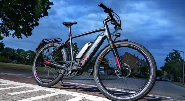 Grijze speed pedelec met bagagedrager en accu, klaar voor een rit. Het kenteken is niet zichtbaar, maar de fiets is wel voorzien van alle benodigde onderdelen.