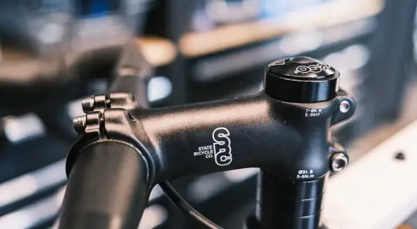 Zwarte fietsstuurpen, merk State Bicycle Co., met spacers om de stuurpen te verhogen voor een comfortabelere fietshouding.