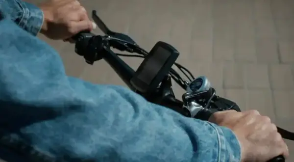 Handen aan het stuur van een elektrische fiets, klaar voor een rit. De aansluiting van de accu is niet zichtbaar, maar de fiets is klaar voor gebruik.