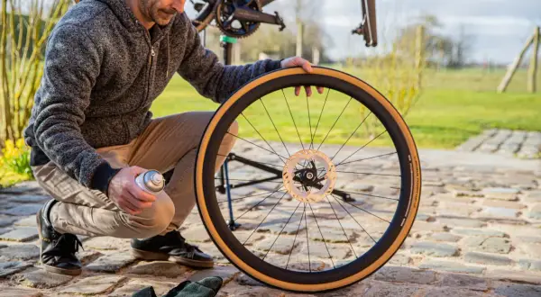 Man onderhoudt fietswiel met remschijf. Hij spuit met een busje, mogelijk voor het handrem fiets afstellen.