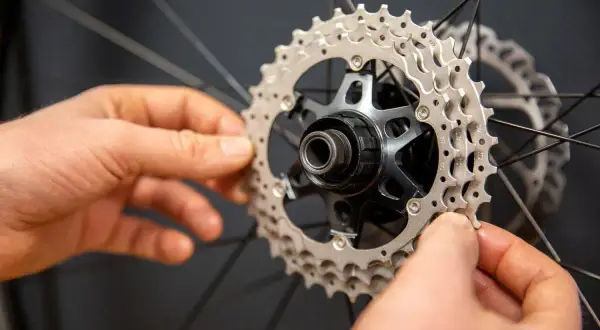 Handen monteren een nieuwe cassette op een fietswiel. Het vervangen van de cassette is een klus die precisie vereist.