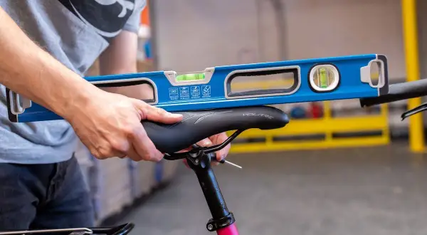 Een persoon gebruikt een waterpas om het fietszadel af te stellen. De waterpas ligt op het zadel om te controleren of het recht staat.