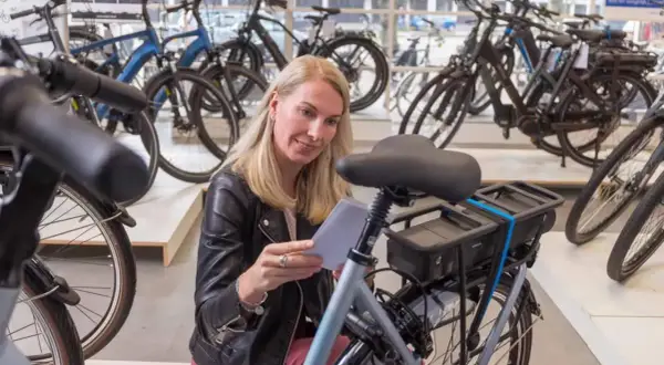 Vrouw overweegt wel of geen elektrische fiets in een fietsenwinkel, omringd door diverse modellen.
