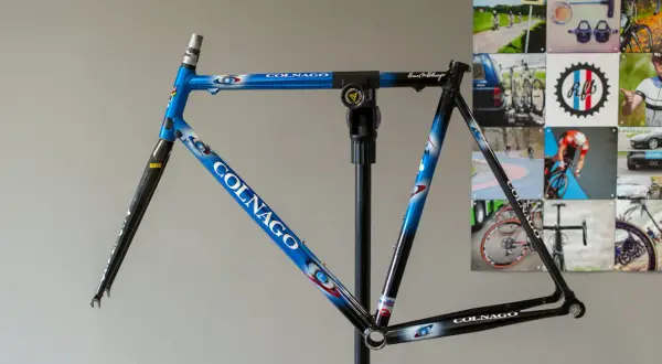 Blauw met witte en rode accenten, een Colnago racefiets frame op een standaard, klaar voor de afmontage.