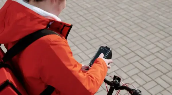 Bezorgbezorger in oranje jas checkt zijn telefoon op de fiets, hopelijk geen boete telefoon fiets!