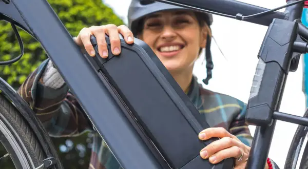Vrolijke vrouw met helm bevestigt de accu van haar e-bike. Goed accu onderhoud zorgt voor zorgeloze fietstochten.