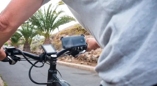 Persoon op een speed pedelec, die een motorvoertuig is, met telefoonhouder en display. Palmbomen op de achtergrond.
