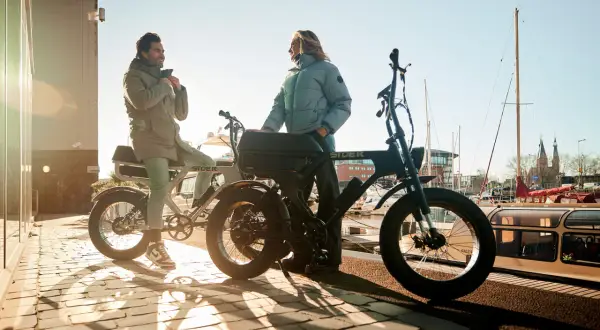 Twee mensen bij hun fatbikes aan het water. De vraag "hoe zwaar is een fatbike" komt op, maar deze stoere e-bikes lijken verrassend licht.
