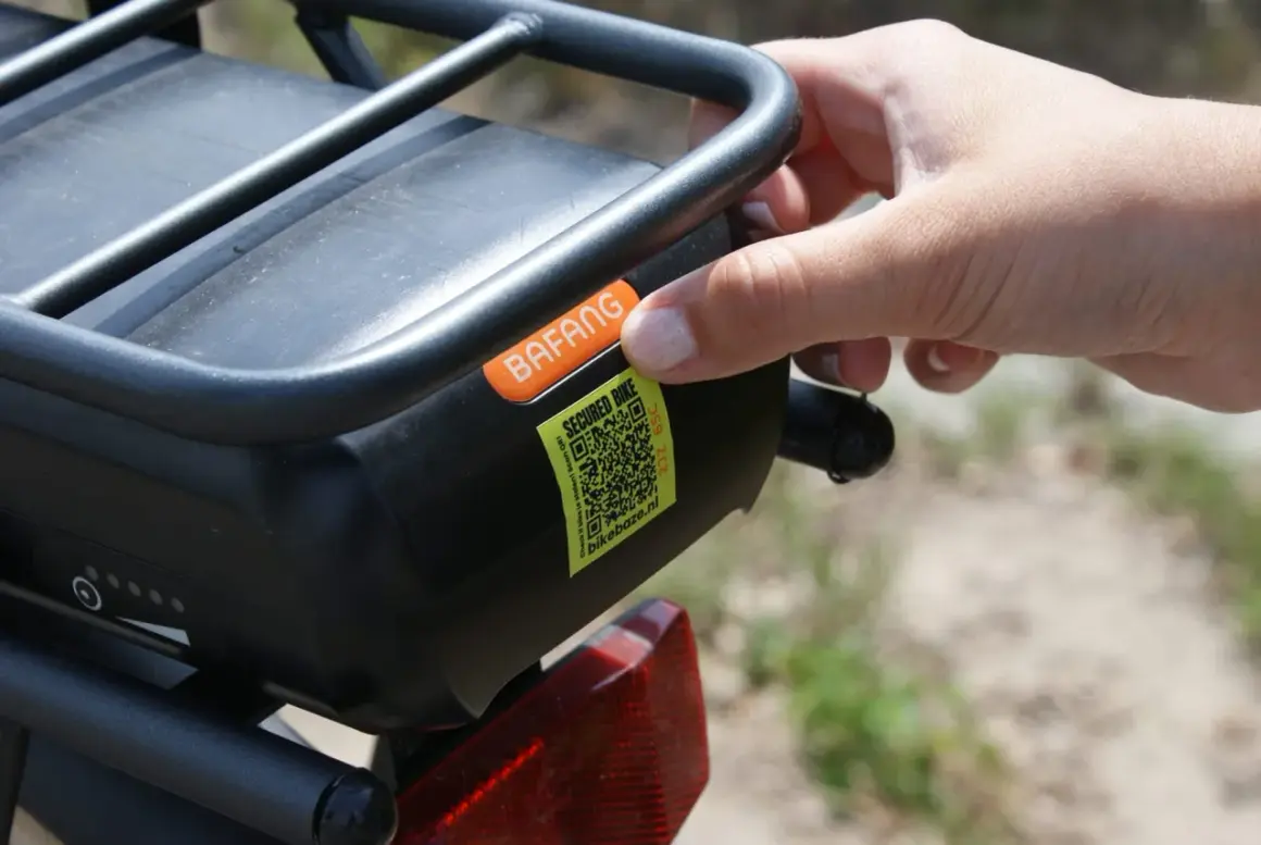 Hand plaatst sticker met QR-code op e-bike accu. Dit is een gestolen fiets register om diefstal te voorkomen.