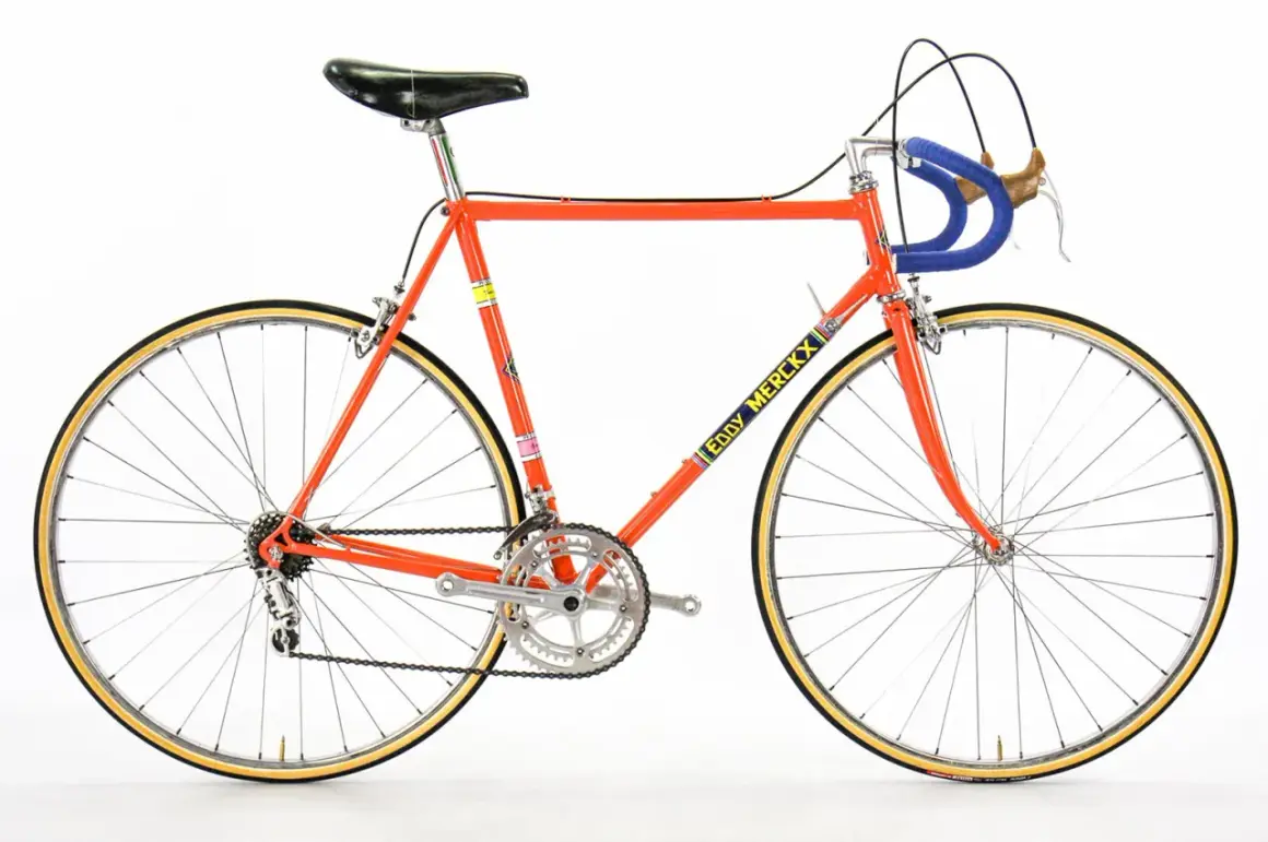 Klassieke racefiets in fel oranje, met "Eddy Merckx" op de buis. Een iconisch stukje fietsgeschiedenis.