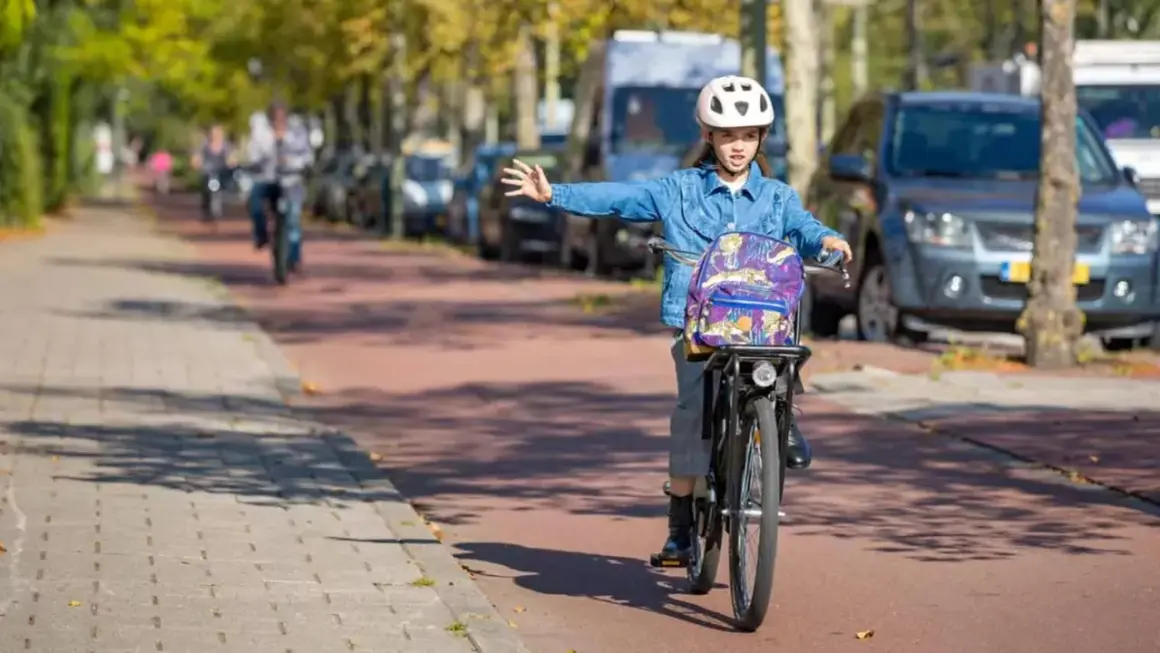 Meisje op fiets met rugzak en helm geeft richting aan, een voorbeeld van verkeersregels voor fietsers.
