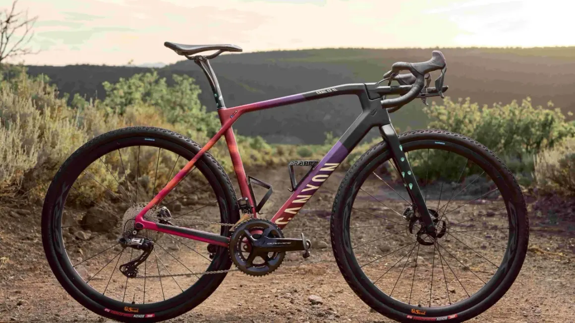 Een kleurrijke Canyon fiets, ideaal voor cyclocross vs gravel bike avonturen, staat in een droog, heuvelachtig landschap.