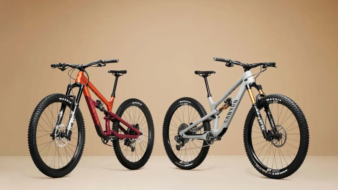 Twee mountainbikes, één oranje/rood en één grijs, met duidelijke wielmaat en Maxxis banden.