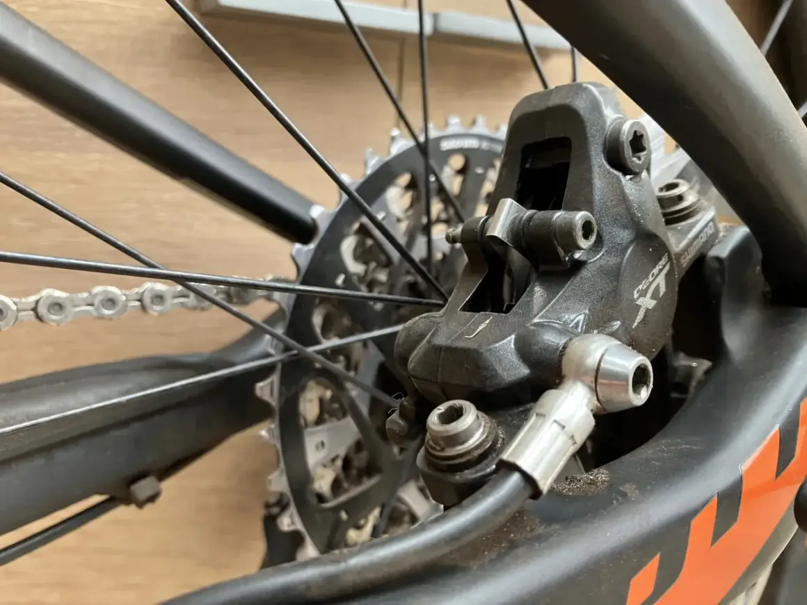 Close-up van een fietsremklauw, klaar voor het bijvullen van hydraulische remmen. De schijfrem en ketting zijn zichtbaar.