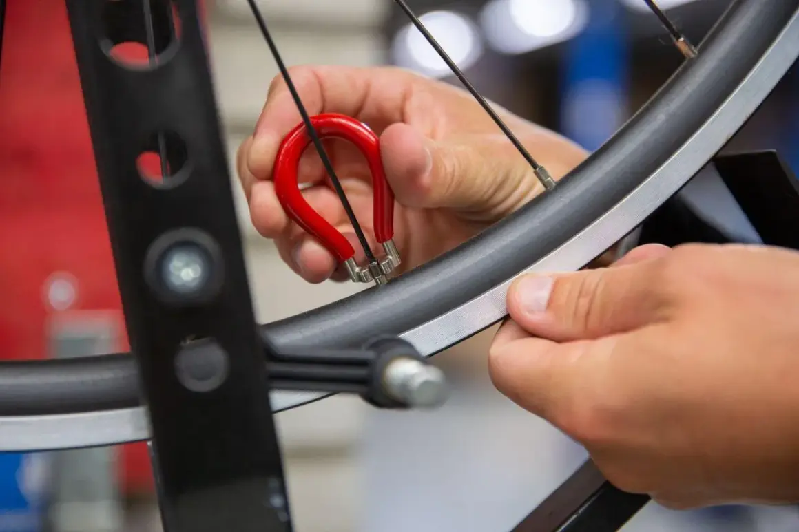 Met een rode spaaksleutel wordt een fietswiel gericht. Een hand draait aan de nippel om het wiel weer perfect rond te maken.