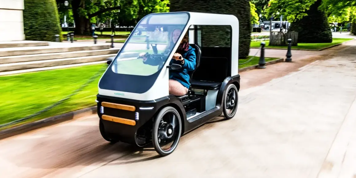 Een vrouw rijdt in een moderne fiets met dak door een park. De fiets heeft een strak design en biedt bescherming tegen het weer.