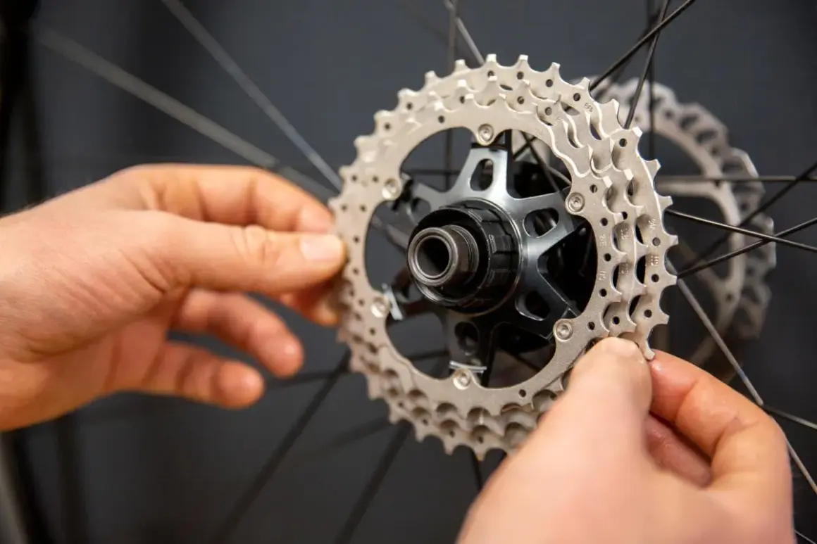 Handen monteren een nieuwe cassette op een fietswiel. Het vervangen van de cassette is een klus die precisie vereist.