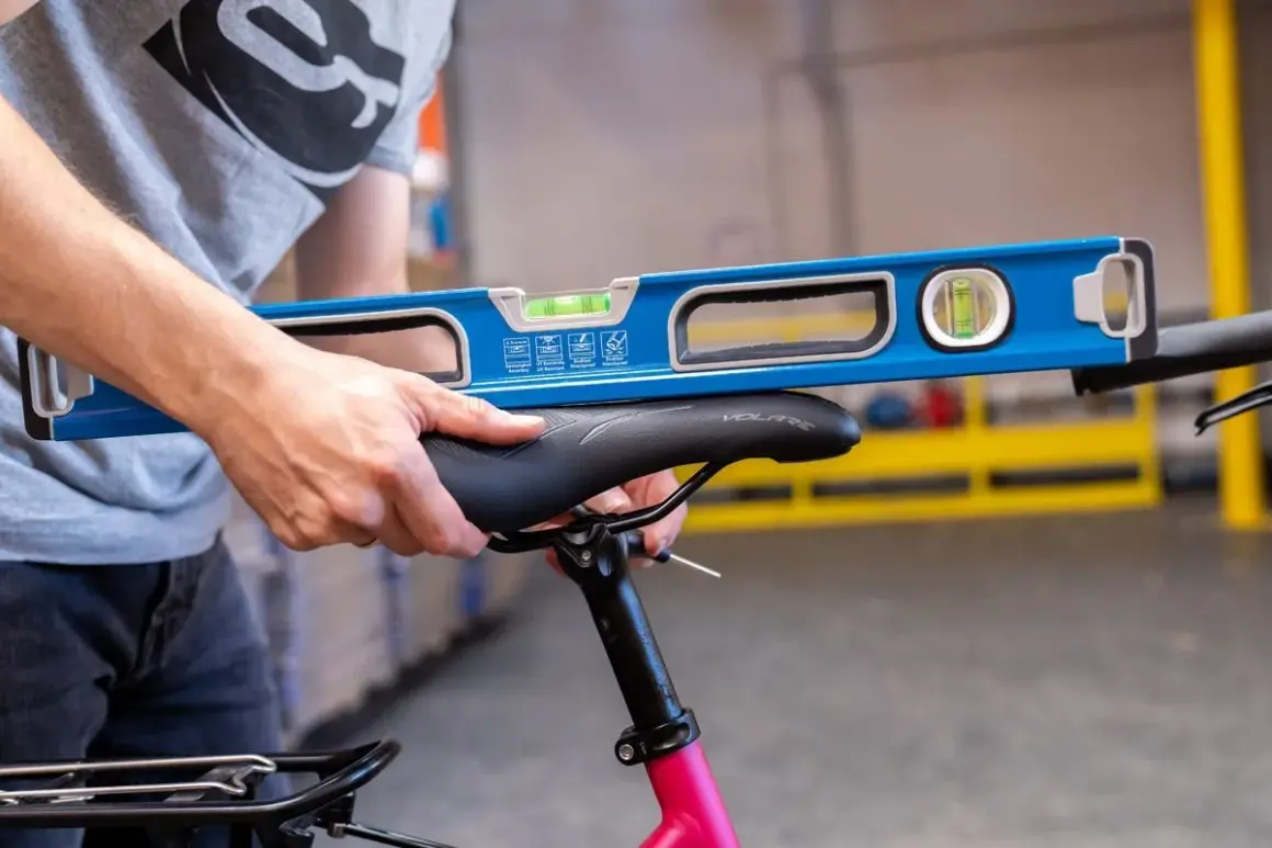 Een persoon gebruikt een waterpas om het fietszadel af te stellen. De waterpas ligt op het zadel om te controleren of het recht staat.