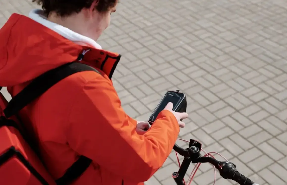 Bezorgbezorger in oranje jas checkt zijn telefoon op de fiets, hopelijk geen boete telefoon fiets!