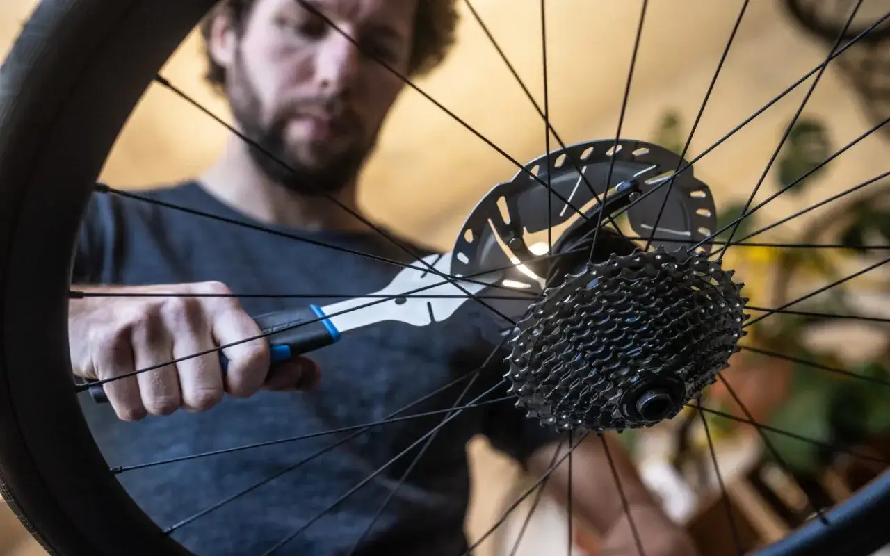 Man met tang aan schijfremmen van fietswiel, bezig met schijfremmen inremmen voor optimale remkracht.