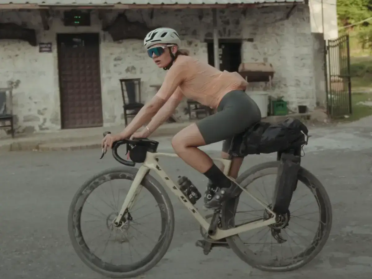 Vrouw op een fiets, klaar voor gesoigneerd wielrennen. Ze draagt een helm, bril en sportkleding, met bagage op de fiets.