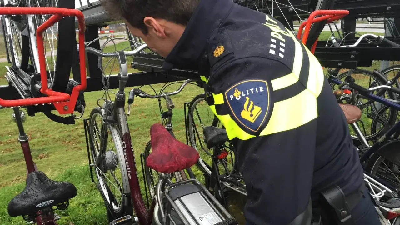 Politieagent controleert fietsen op diefstal preventie chip. De agent draagt een uniform met het woord 'Politie'.