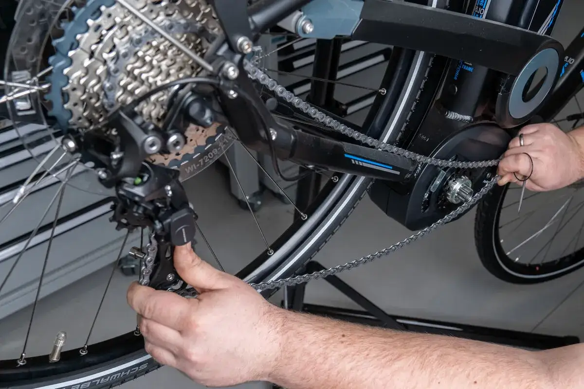 Handen werken aan de ketting van een elektrische fiets. Het tandwiel fiets vervangen is een klus die geduld vereist.
