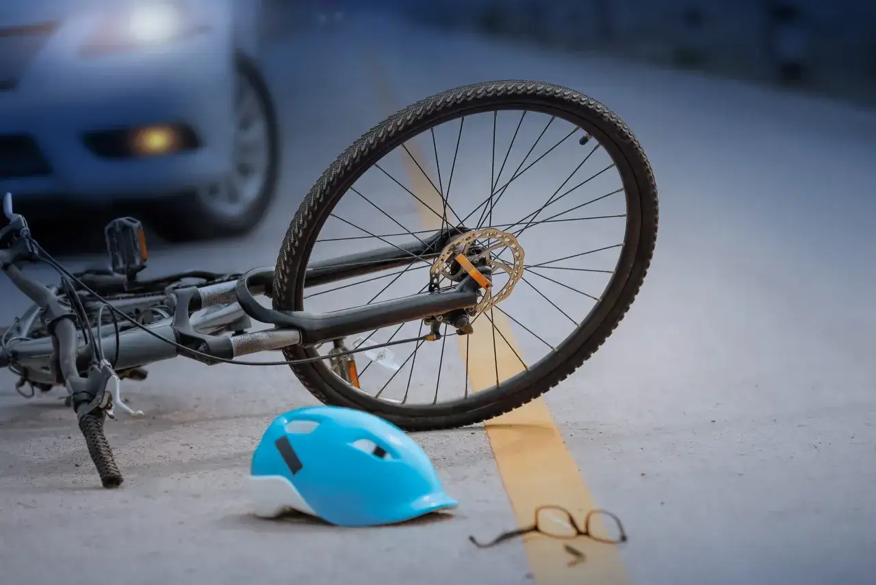 Fiets, helm en bril liggen op straat na een aanrijding. Een auto op de achtergrond suggereert een ongeval, mogelijk met smartengeld aanrijding fiets als gevolg.