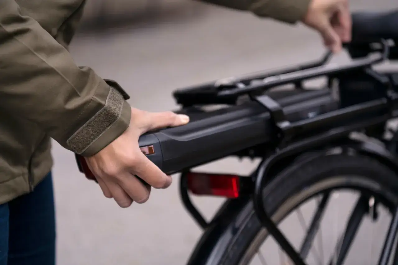 Hand verwijdert de accu van een elektrische fiets in een schuur, klaar voor opladen.