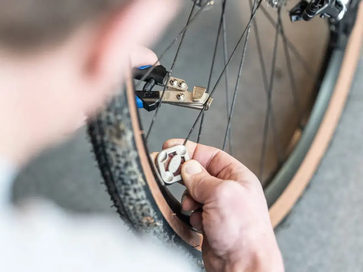 Een hand gebruikt een spakenspanner om een fietswiel te richten.